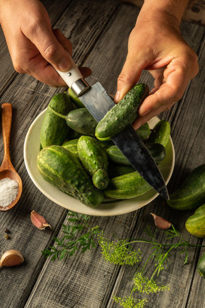 Hands are skillfully slicing fresh cucumbers on a wooden table, surrounded by herbs and garlic, highlighting the vibrant colors and textures of the ingredients.の写真素材