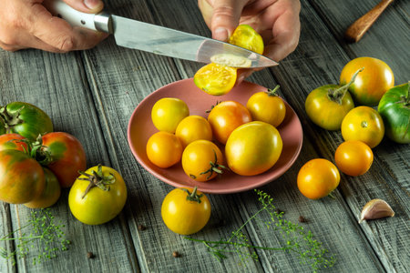 Hands skillfully slice ripe tomatoes on a wooden table, surrounded by an assortment of colorful...