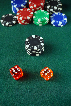 Two dice red sit in front of a stack of black poker chips, with various colored chips arranged...