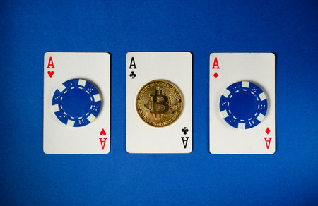 Three playing cards with aces and blue chips surround a golden bitcoin on a blue surface, creating a...