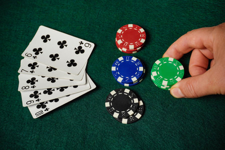 Players engage in a friendly card game, with a hand of club cards and various colored poker chips on...