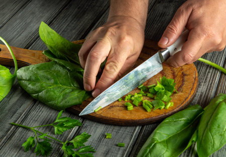 Hands skillfully chop fresh spinach and green onions on a wooden cutting board. The scene captures the essence of healthy cooking and meal preparation at home.の写真素材
