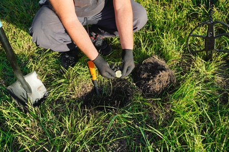 A person wearing gloves holds a small item found with a metal detector while digging in a grassy...