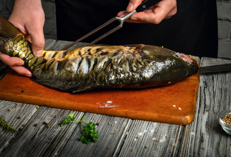 A person skillfully holds a large fish on a wooden cutting board, preparing it for cooking. Fresh...