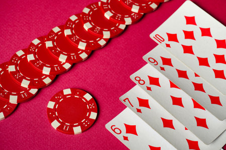 The photograph shows a close-up of red poker chips neatly arranged next to playing cards depicting a winning straight flush.の写真素材