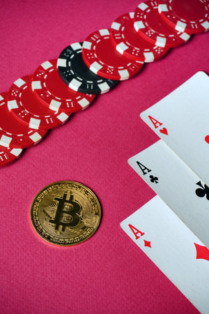 Red and black poker chips line a pink table next to three aces and a Bitcoin coin, showing the combination of classic games and modern digital currency.の写真素材