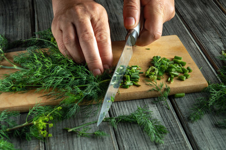 Hands skillfully chop vibrant green herbs on a wooden cutting board, surrounded by fresh ingredients in a cozy kitchen. A culinary scene full of flavor and creativity.の写真素材