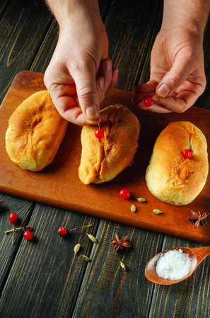 Hands carefully place viburnum on freshly baked sweet buns placed on a wooden board. Spices and salt surround the buns, creating a warm kitchen atmosphere.の写真素材