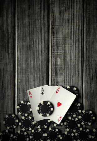 Three aces, or a three-of-a-kind hand, lie on a stack of black poker chips. The rustic wooden table creates a classic casino atmosphere.の写真素材