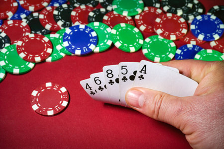 A person holds a hand of cards while surrounded by colorful poker chips in shades of red, blue, and...