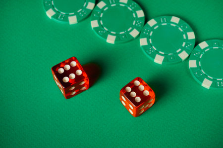 Red dice are rolled on a green gaming table alongside several green poker chips. The scene captures the thrill of a casino atmosphere filled with anticipation.の写真素材
