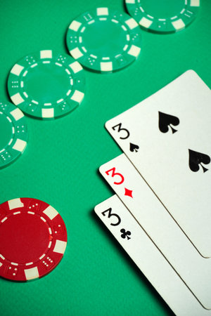 Three playing cards depicting three of a kind or set lie next to several multicolored poker chips on...