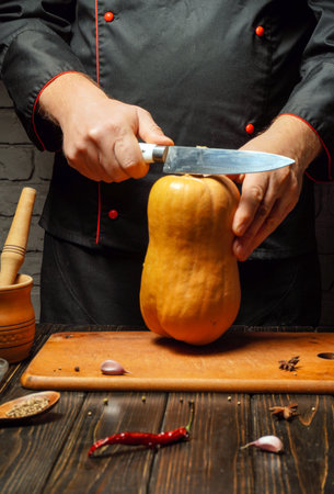 A chef is expertly cutting a fresh butternut squash on a wooden cutting board in a rustic kitchen. The atmosphere is warm with simple cooking utensils displayed.の写真素材