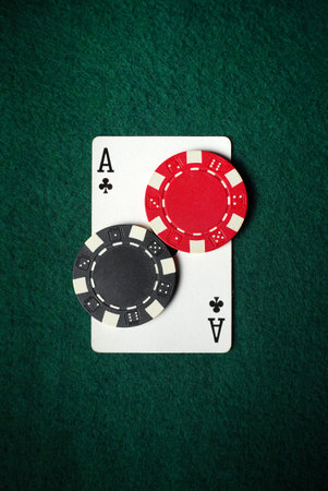 Two poker chips, one red and one black, sit on top of an Ace of clubs card on a green felt table,...