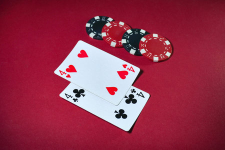 Two playing cards depicting four hearts and four clubs lie next to several poker chips on a red...