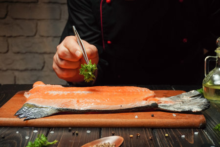 A chef carefully arranges herbs on a raw salmon fillet while working in a warm, inviting kitchen. Soft lighting creates a relaxing ambiance in the space.の写真素材