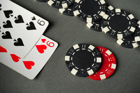 A set of black and red poker chips sits next to two playing cards marked with hearts and spades....