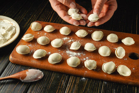 In a warm kitchen, hands are skillfully shaping dumplings on a wooden board sprinkled with flour....