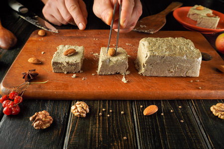 Hands carefully cut and shape traditional nut candy on a wooden board, surrounded by fresh ingredients like almonds and walnuts. Sweet aroma fills the cozy kitchen.の写真素材