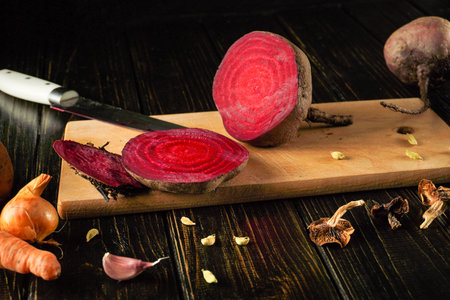 Bright red beets are sliced on a wooden cutting board, showing their vivid color. Nearby, fresh...