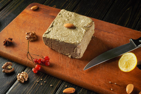 A block of rich nut-based spread rests or halva on a wooden cutting board. Garnished with almonds,...