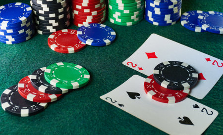 Colorful poker chips are stacked next to playing cards featuring deuces or one pair on a green felt...