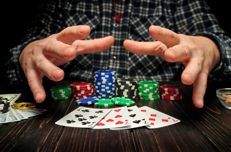 Hands of a person reach over a table with poker chips stacked high next to playing cards. Dollar bills are visible in the background, indicating a gambling scene.の写真素材