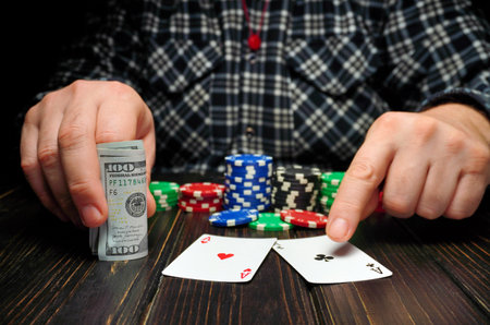 A person is focused on a card game, holding two playing cards and a stack of poker chips. A roll of...