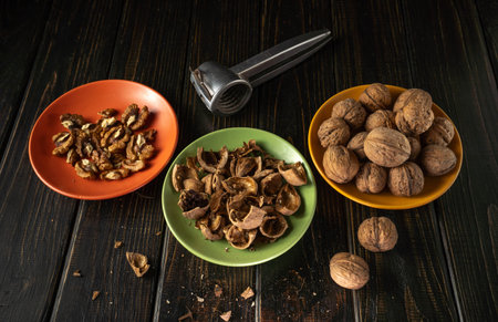 Three plates are arranged on a dark wooden table. One plate holds shelled walnuts, another has...