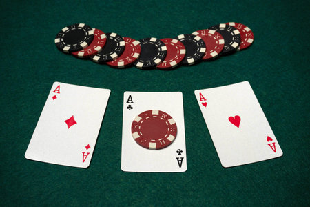 Cards are placed face up on a green table, showing three aces. Poker chips are stacked in the...