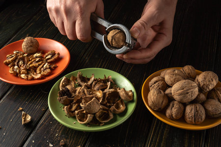A person uses a nutcracker to break open walnuts. The opened nuts are placed on a green plate, while...