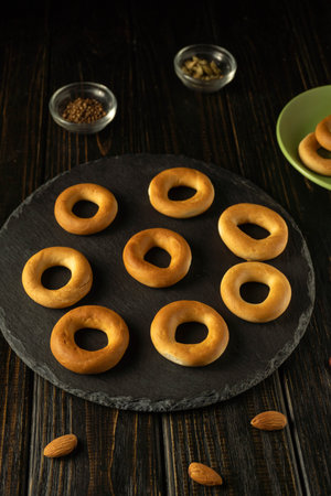 Baked rings of dough rest on a black stone plate or bublik. Small bowls with spices are nearby, and...
