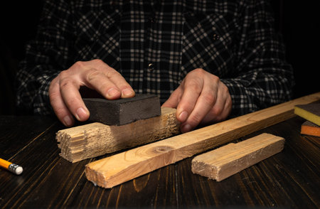 A person is sanding wood to smooth its surface. The hands hold sandpaper against a piece of wood....
