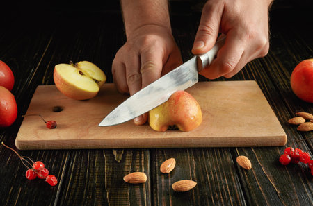 A person is slicing fresh, red apples on a wooden cutting board. Almonds and bright red berries are...