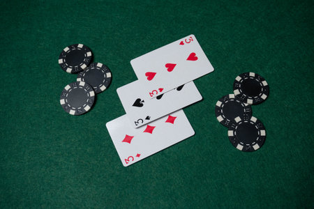 Three playing cards lie on a green felt table next to black poker chips. A poker game is in progress...