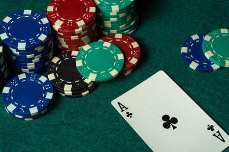 Several stacks of poker chips lie on a green table, and an Ace of Clubs card lies next to it. All...
