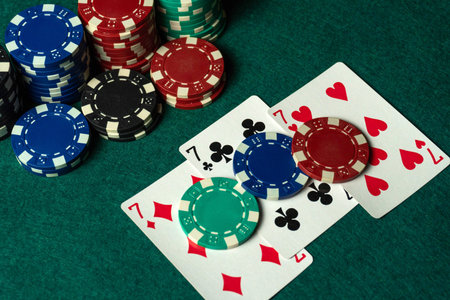 Three of a kind or set of playing cards are placed next to several stacks of poker chips on a green...
