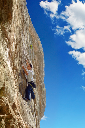Young man climbs on a rocky wall, against a blue skyの写真素材