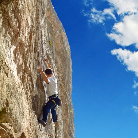 Young man climbs on a rocky wall, against a blue skyの写真素材
