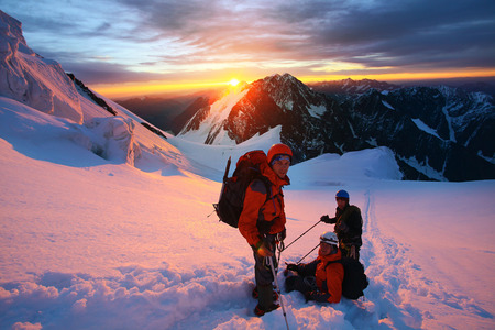 climbers at the top of a pass with backpacks meeting the sunrise in the mountainsの写真素材