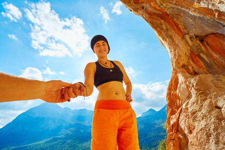 girl climber standing in a cave under arch on blue cloudy sky background and looking at the camera.の写真素材