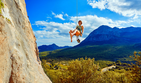 female rock climber hanging on a rope near the rocky wall on the mountain backgroundの写真素材