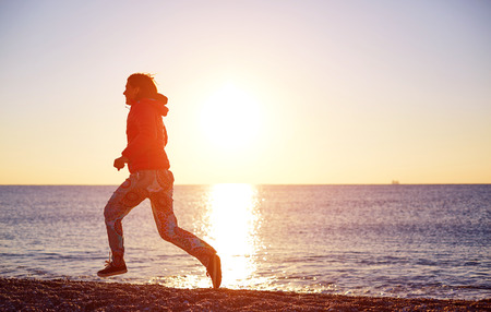 happy girl running on the beach at sunrise against the sun. silhouetteの写真素材