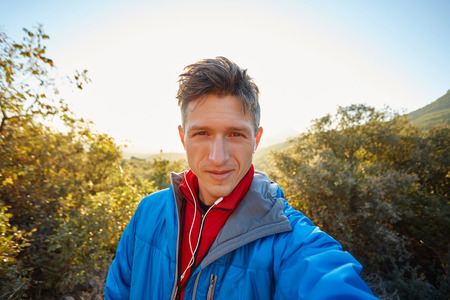 young  man make selfie on the morning mountains background. Man dressed in a blue blazer and a red jacketの写真素材
