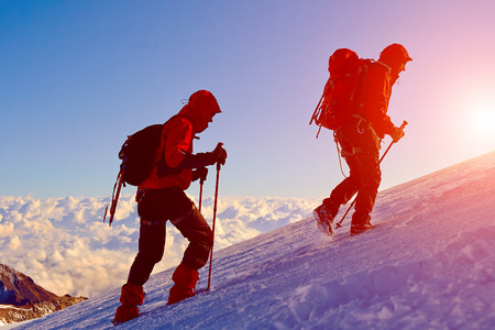 climbers at the top of a pass with backpacks meeting the sunrise in the mountainsの写真素材