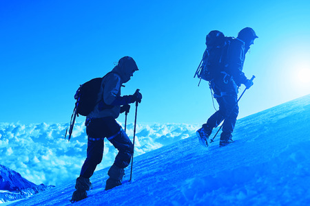 climbers at the top of a pass with backpacks meeting the sunrise in the mountainsの写真素材