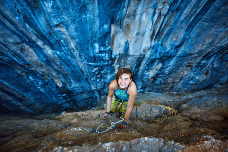 female rock climber climbs on a rocky wall, Keep a hand on the rock and laughs.の写真素材