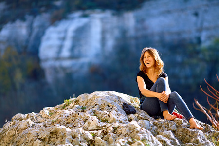laughing woman  looks into the camera on the rocks at sunsetの写真素材