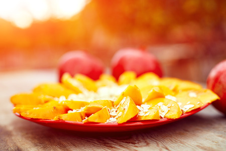 Sliced fruits arrangement. Delicious Persimmon fruit with bananas and oat-flakes ready to serve. laid out on a red plate on a wooden background.の写真素材