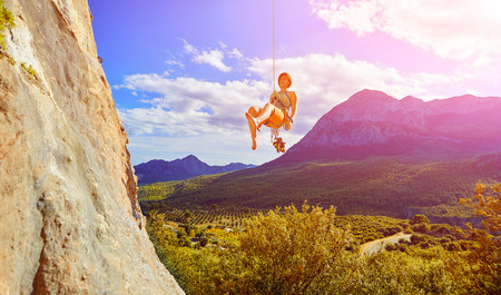 female rock climber hanging on a rope near the rocky wall on the mountain backgroundの写真素材